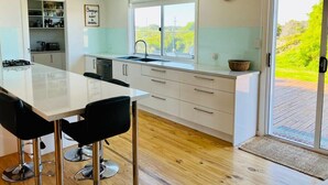 A modern kitchen with a central island, white cabinetry, a large window, and a view of greenery outside. - C4 Miles - Wood Fire - Sea Views - RC/AC (Robe)