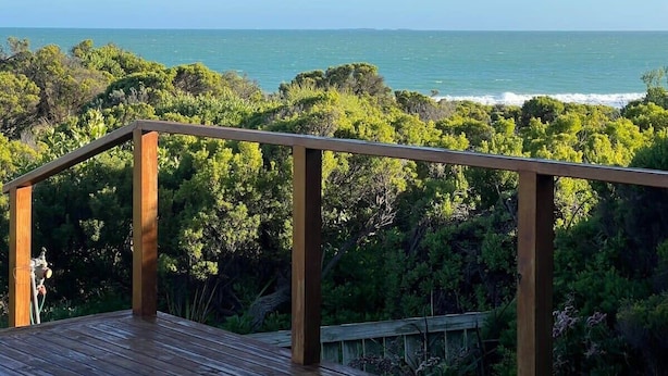 A wooden deck with a railing overlooking a coastal landscape with dense greenery and the sea. - C4 Miles - Wood Fire - Sea Views - RC/AC (Robe)