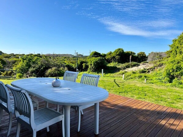 Une table ronde entourée de chaises, posée sur une terrasse en bois, le tout agrémenté de verdure et surplombant des collines.