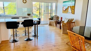 A modern kitchen with a dining area, wooden flooring, and a large window with a view. - C4 Miles - Wood Fire - Sea Views - RC/AC (Robe)