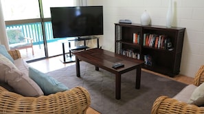 A living room with a TV, bookshelf, wicker furniture, and a balcony.