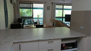 Een keuken met een marmeren aanrecht, witte kastjes, een magnetron en een eethoek met stoelen en een tafel.