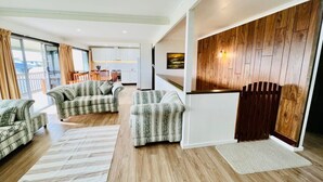 Uma sala de estar moderna com um conjunto de sofá, piso de madeira e uma cozinha ao fundo.