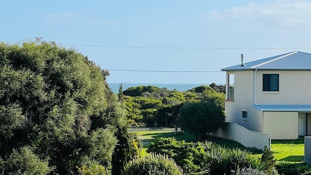 Uma casa moderna de dois andares com telhado plano, cercada por vegetação exuberante e céu claro.