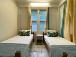 A small, clean room with two single beds, a small table, and a window with curtains.