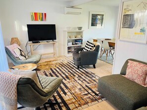 A living room with a flat-screen TV, two armchairs, a sofa, a coffee table, a patterned rug, and a bookshelf. - No.34 - Pet Friendly outside (Robe)