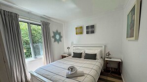 A bedroom with a bed, bedside tables, a mirror, and a view of greenery outside.