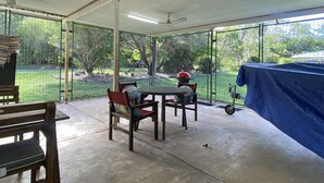 A covered patio area with a round table and chairs, a grill, and a view of a fenced yard. - Whitehaven 2 (Picnic Bay)