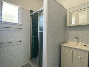Een badkamer met een douche, wastafel en kastjes.