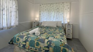 A bedroom with a bed, curtains, bedside tables, and a lamp. - Whitehaven 2 (Picnic Bay)