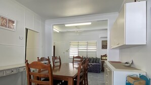 A dining area with a wooden table and chairs, a kitchenette with a white cabinet, and a window with blinds. - Whitehaven 2 (Picnic Bay)
