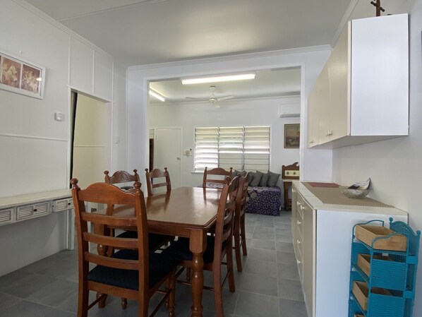 A dining area with a wooden table and chairs, a kitchenette with a white cabinet, and a window with blinds.