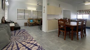 A living room with a sofa, a dining table with chairs, a kitchen area, and a window with blinds. - Whitehaven 2 (Picnic Bay)