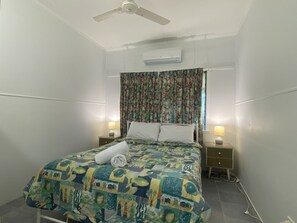 Een slaapkamer met een bed, twee nachtkastjes met lampen, een plafondventilator en een airconditioning.