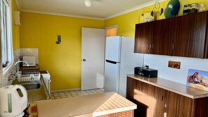 Une cuisine de taille réduite, avec un réfrigérateur blanc, des placards en bois, un évier et une bouilloire.