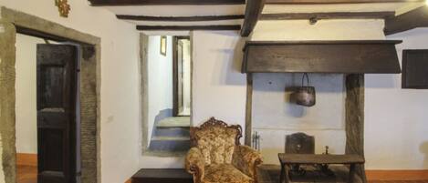 A room with a wooden ceiling, a chair, a fireplace, and a door.