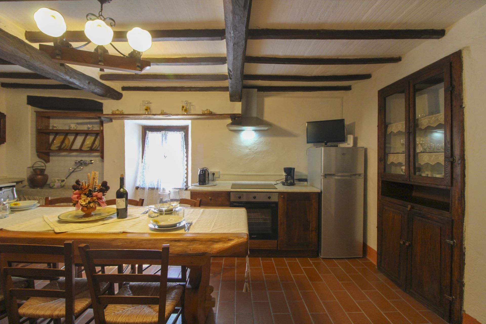Een keuken met een eettafel, stoelen, een koelkast, een fornuis en een raam.