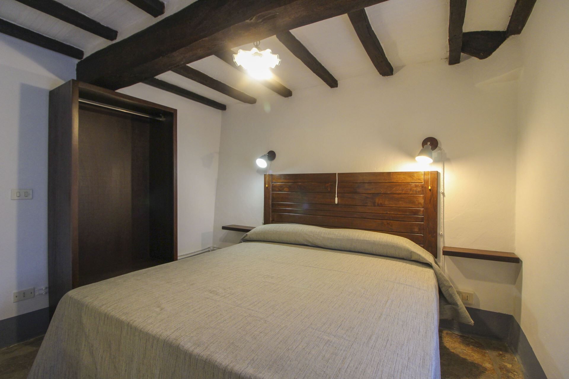 A bedroom with a wooden headboard, a bed with a light-colored bedspread, and two bedside lamps.