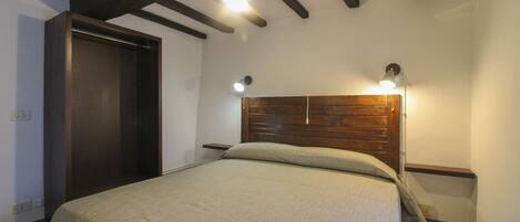 A bedroom with a wooden headboard, a bed with a light-colored bedspread, and two bedside lamps.