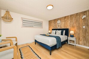 A bedroom with a bed, bedside tables, a hanging light fixture, a wall-mounted mirror, and a wooden accent wall. - Relaxing Lakeside Bungalow,Steps to Lake Samish Park to enjoy lake activities (Bellingham)