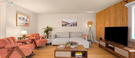A living room with a sofa, two armchairs, a coffee table, a TV, and a lamp.