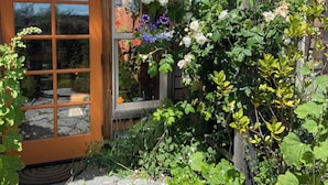 Une maison en bois avec une porte et des fenêtres en verre, entourée d’une végétation luxuriante et de plantes en fleurs.