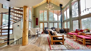Un amplio salón con escaleras de madera, ventanas grandes y una chimenea.