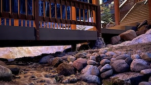 Un puente de madera sobre un arroyo con rocas, un suelo de madera y una escalera que lleva a un nivel superior.