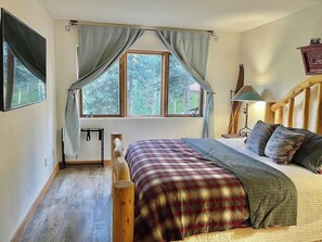 A bedroom with a bed, a window with curtains, a bedside lamp, and a wooden headboard.