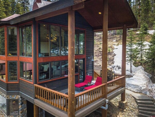 A wooden cabin with large windows and a deck area with red seating.