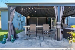 Relax in this serene outdoor patio with a table and two chairs, surrounded by a metal roof and string lights.