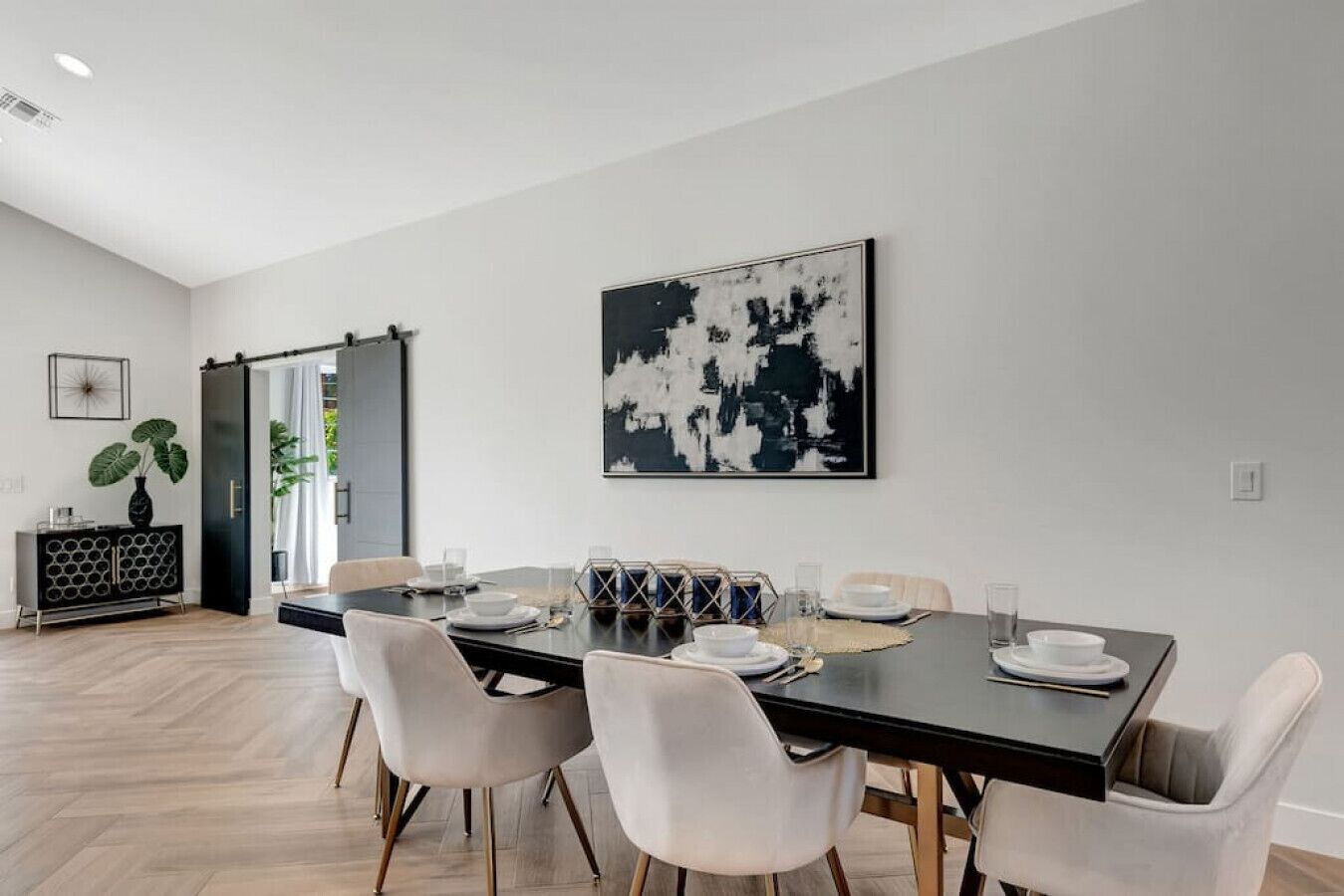 A modern dining room with a black table, white chairs, and a large abstract painting on the wall.