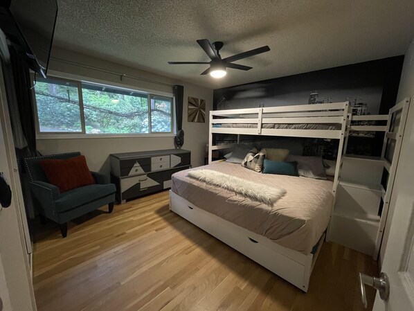 A bedroom with a bunk bed, a sofa, a desk, and a window with a view of trees.