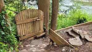 Een houten poort die uitkomt op een pad van stenen, omgeven door bomen en een beekje.