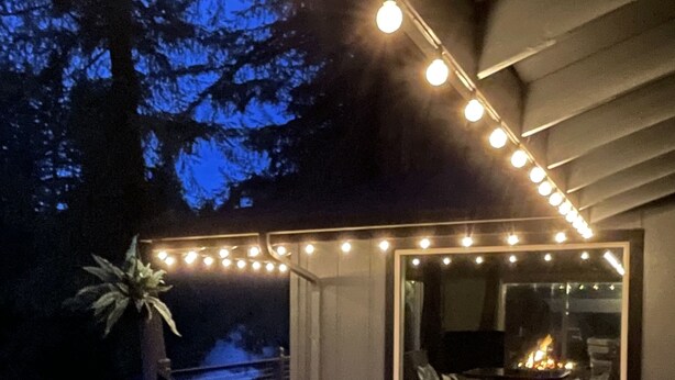 Een terras met lichtjes, een vuurplaats en uitzicht op bomen.