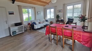 Una habitació acollidora amb sostre de fusta, una taula de dinar amb cadires, un sofà i una taula petita amb una làmpada.