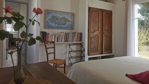 Un dormitori amb un llit de fusta, una biblioteca amb llibres, un mapa a la paret i una finestra que mostra vistes a la vegetació.
