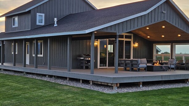 Ein zweistöckiges Haus mit überdachter Veranda, Sitzgelegenheiten im Freien und Grillplatz.