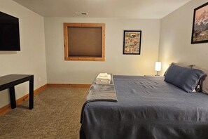 A bedroom with a bed, a nightstand, a window with blinds, a wall-mounted TV, and a framed poster. - Alpenglo Farm with Event Space and Parking (Driggs)