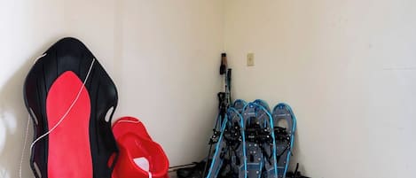 Un coin de pièce avec un mur blanc, un objet rouge et noir appuyé contre ce mur, et une paire de skis bleus et noirs adossés au mur.