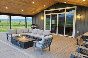 A covered outdoor seating area with a fire feature, a grill, and a view of a green landscape.