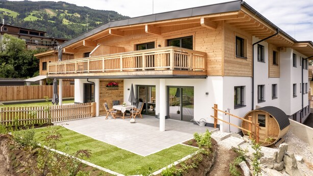 Une maison moderne à deux étages, dotée d’un balcon en bois, d’un patio couvert et offrant une vue sur les collines environnantes.