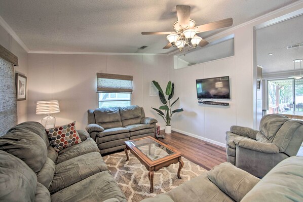 A living room with a ceiling fan, a glass coffee table, and a large window with blinds. - Lakefront Mabank Gem w/ Sunset Views: Pets Welcome (Mabank)