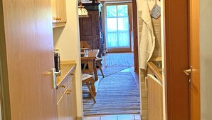 Un pasillo estrecho con armarios de madera, suelo de baldosas y una puerta de madera a la derecha.