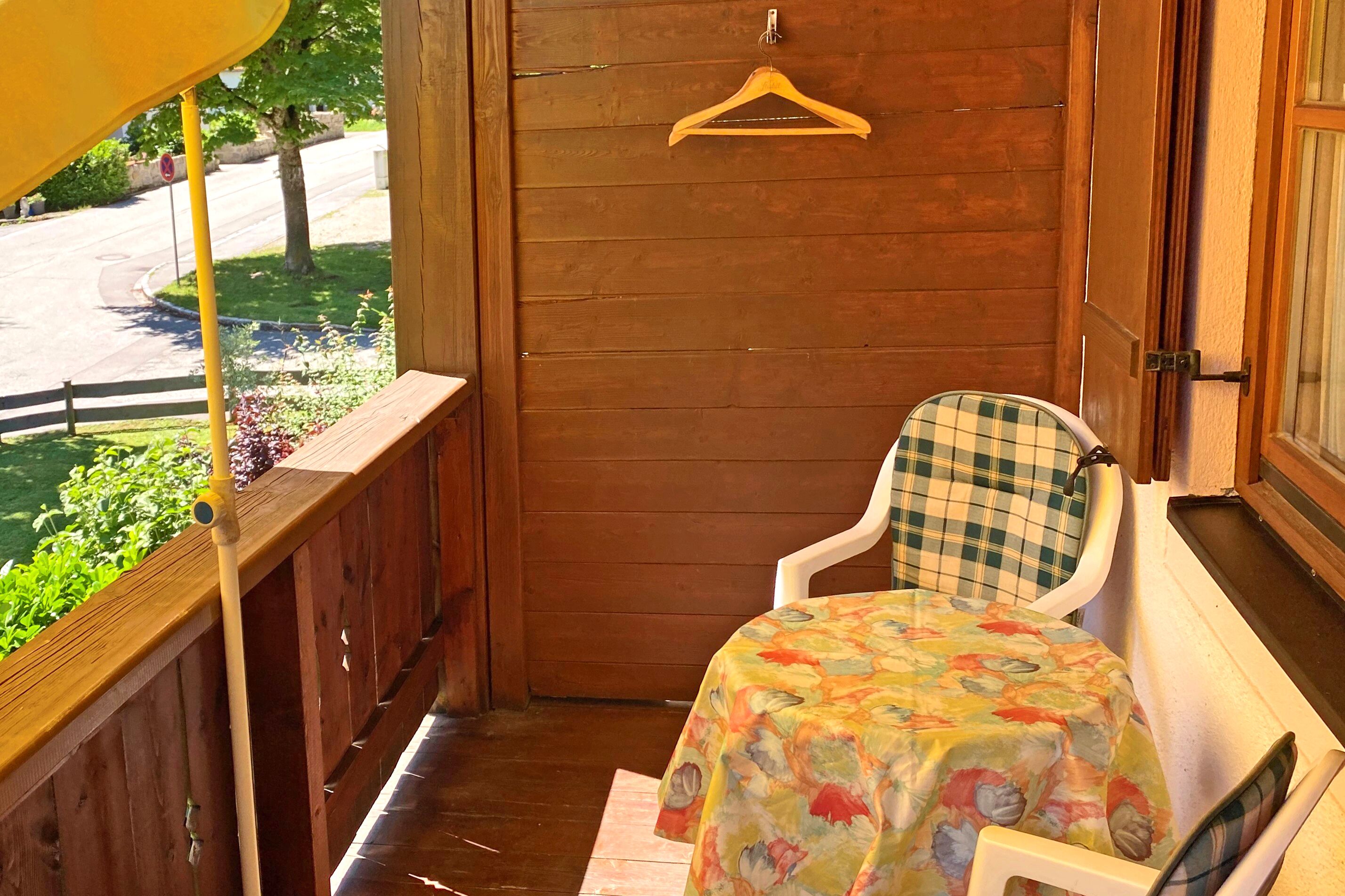 Une véranda en bois avec une table et une chaise, un porte-manteau suspendu et une vue sur la rue.