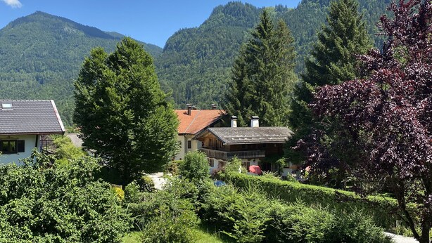 Un pueblo de montaña con casas de madera tradicionales, exuberante vegetación y un cielo azul despejado.