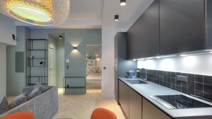 A modern kitchen with dark cabinets, a black tiled backsplash, and a built-in stove. There is a dining area with a glass table and orange chairs. - Charming Flat Saleya OLD Town (Nice)