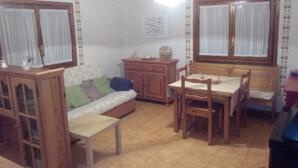 A cozy living room with a sofa, wooden cabinet, dining table with chairs, and a small table with a vase.
