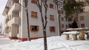 A multi-story building with balconies and wooden windows, surrounded by snow-covered ground and bare trees.