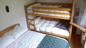 A bunk bed with a lower bunk and a single bed. There is a wooden headboard, a wall-mounted light fixture, and a window with a wooden frame.